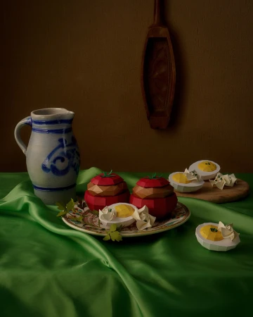 Still life of two tomato-shaped containers and egg halves on a green silk tablecloth, featuring a pitcher and wooden spoon in the background.