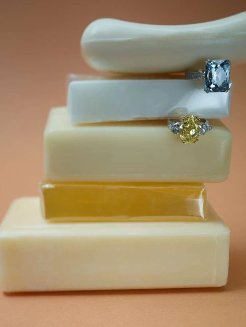 Two gemstone rings are stacked on bars of soap, featuring a blue gemstone on top and a yellow gemstone ring placed below it.