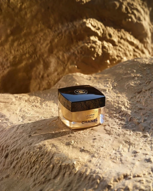 A jar of Chanel skincare product is displayed on a beige, rocky surface, highlighted by warm, natural lighting, enhancing its luxury.