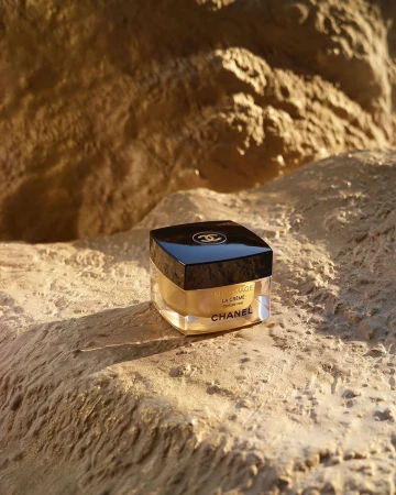A jar of Chanel skincare product is displayed on a beige, rocky surface, highlighted by warm, natural lighting, enhancing its luxury.