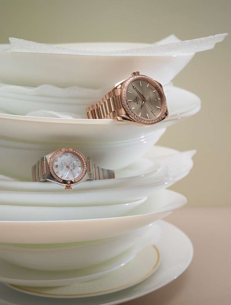 Two rose gold wristwatches are staged on a stack of white plates, emphasizing luxury and unique product placement against a neutral background.