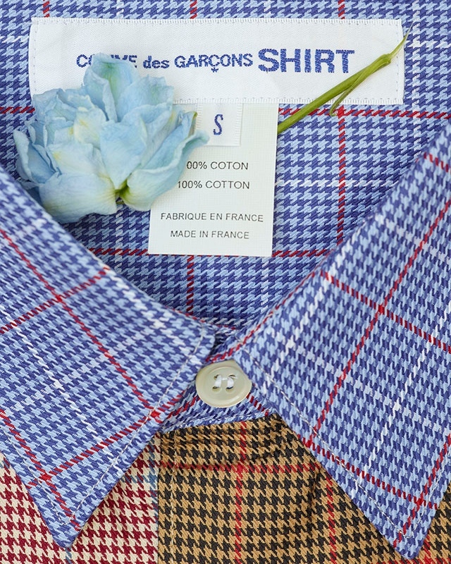 Houndstooth patterned button-down shirt with collar, brand label, and small blue flower detail close up, full-frame fashion stock.