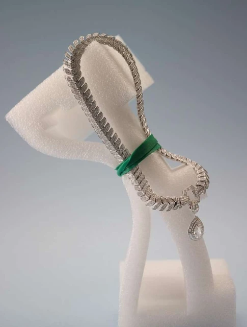 Elegant diamond necklace on a white display stand, photographed in a studio setting against a light blue backdrop. Jewelry advertisement.