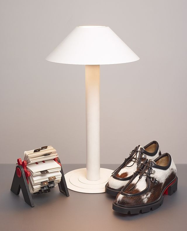 A pair of brown and white shoes sit on a gray surface next to a white lamp and a black and red business card holder.