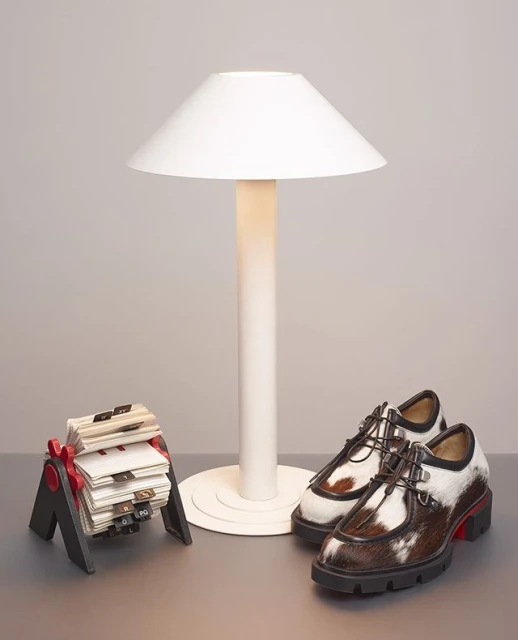A pair of brown and white shoes sit on a gray surface next to a white lamp and a black and red business card holder.