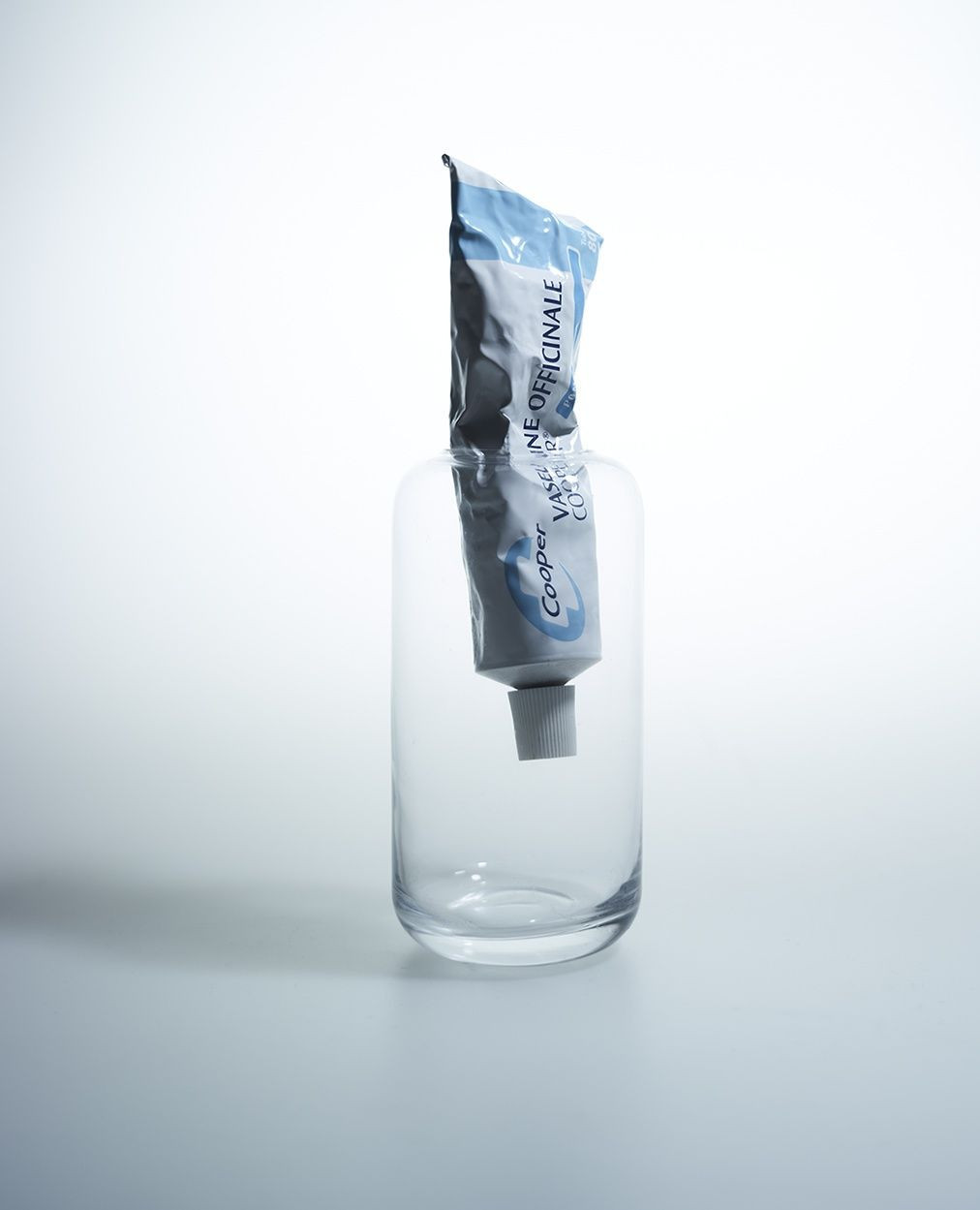 Toothpaste tube inside a glass container on a white surface, product shot highlighting healthcare or dental hygiene concepts.