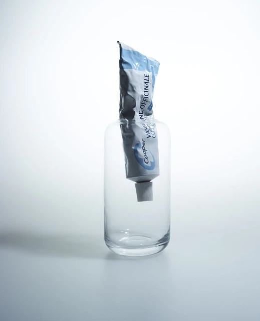 Toothpaste tube inside a glass container on a white surface, product shot highlighting healthcare or dental hygiene concepts.