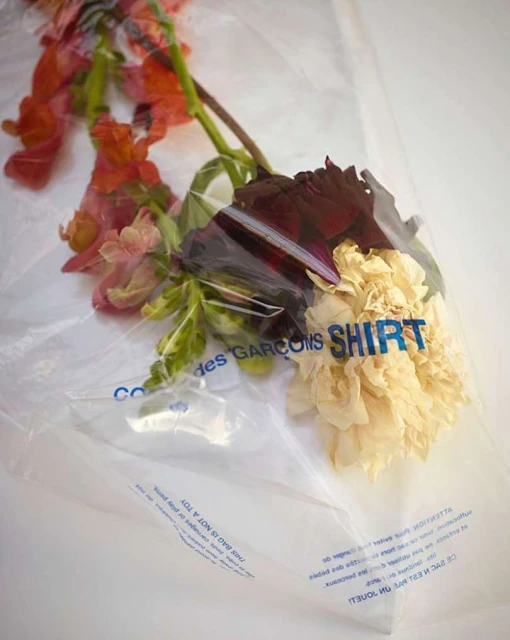 Bouquet of assorted flowers wrapped in a plastic bag with printed text, featuring shades of orange, red, cream, and green.