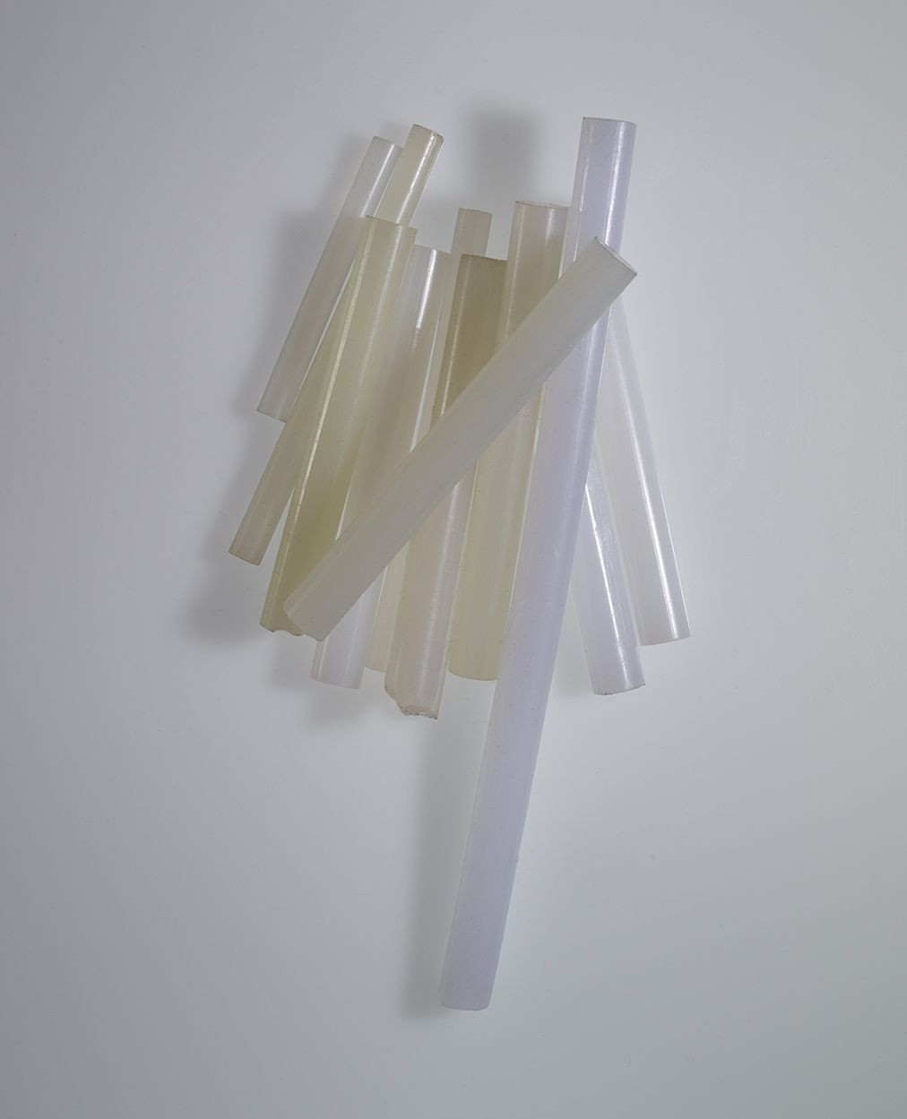 Pile of translucent, cylindrical glue sticks in a vertical arrangement on a plain white surface with subtle gradient lighting.