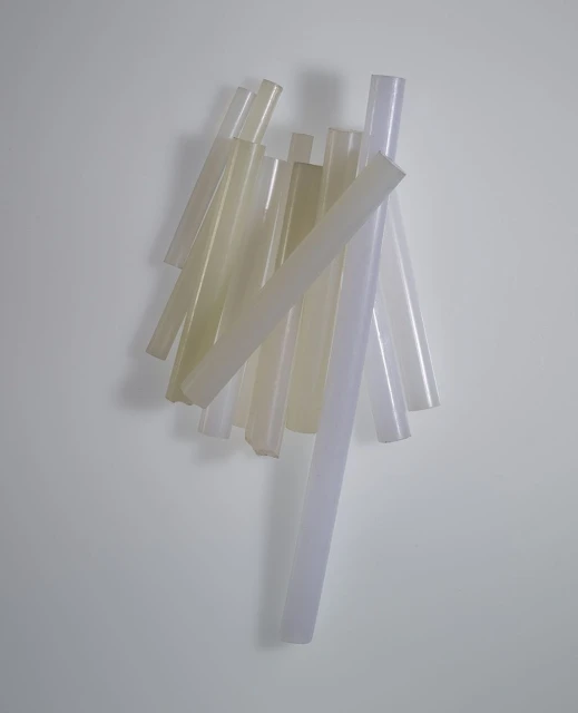 Pile of translucent, cylindrical glue sticks in a vertical arrangement on a plain white surface with subtle gradient lighting.