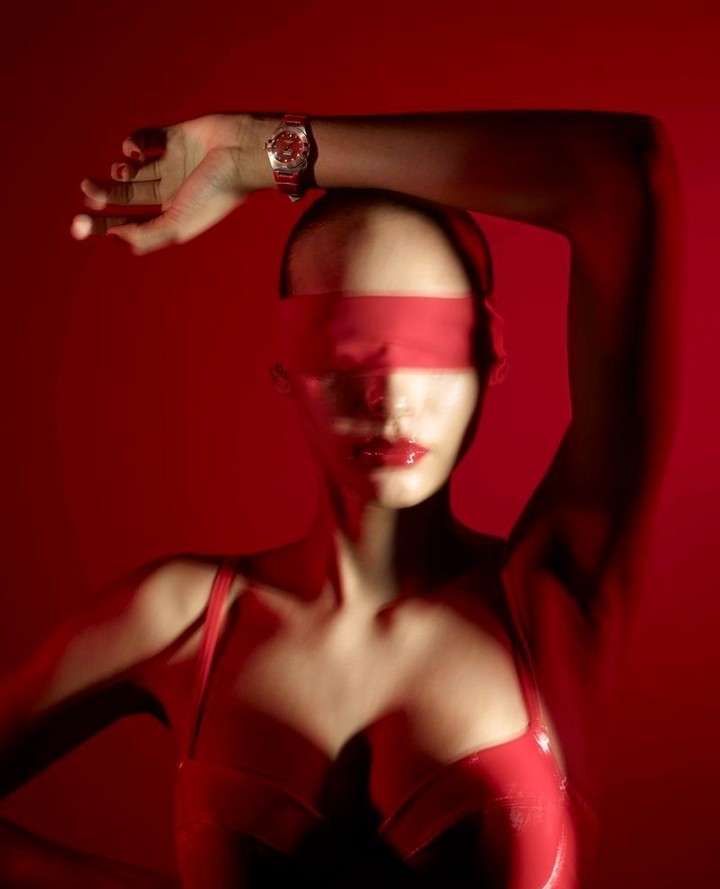 Stylish portrait of a female fashion model in a red monochromatic setting, wearing a red band over her eyes and shiny lipstick.