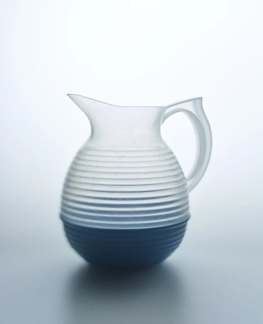 Studio shot of a clear glass pitcher with blue base and grooved design, set against a bright, neutral backdrop showcasing minimalist design.
