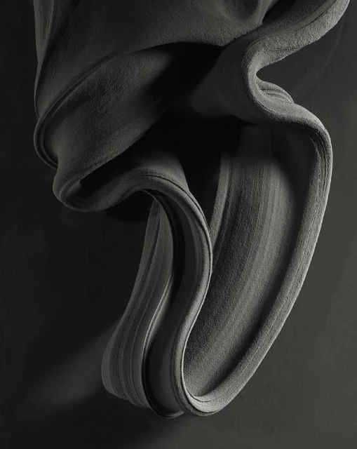 Abstract gray fabric drapes and swirls against a dark gray backdrop, creating a textured, monochrome artistic composition.