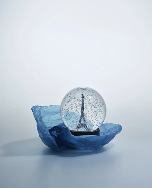 Eiffel Tower souvenir snow globe sits on blue paper, capturing a miniature Paris landmark in a classic travel keepsake.