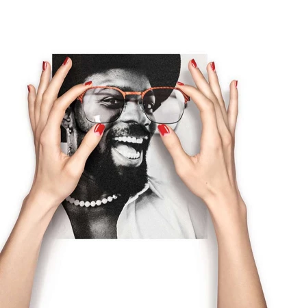 Two hands with red nail polish holding up optical frames in front of a black and white portrait of a smiling man.