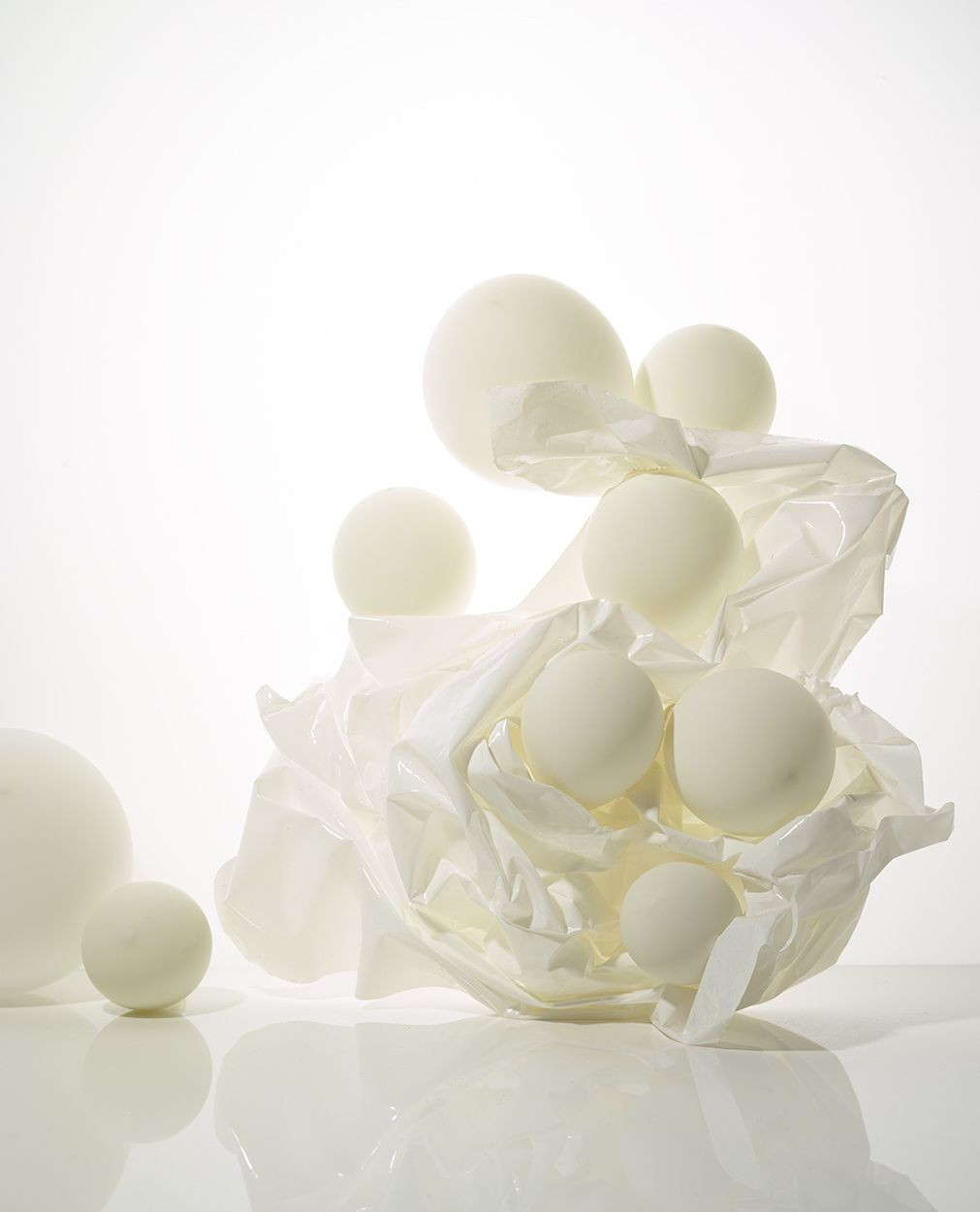 Spherical bath bombs rest on a crumpled white surface in a clean, minimalist composition with soft lighting and light color palette.
