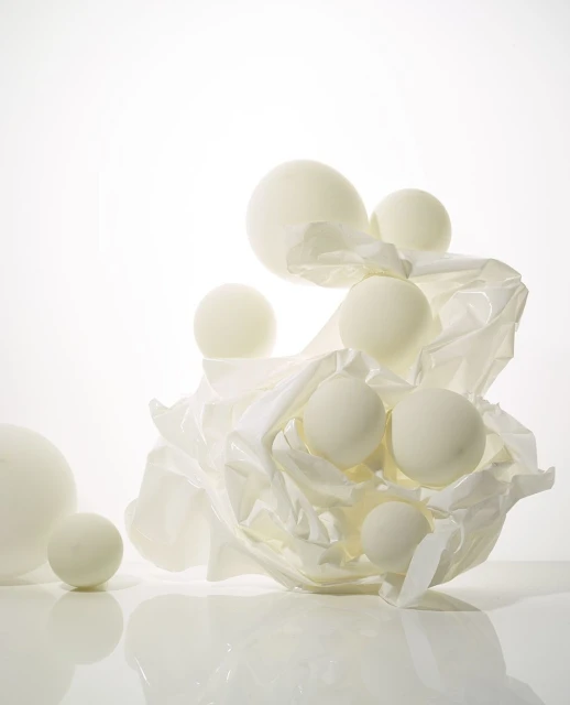 Spherical bath bombs rest on a crumpled white surface in a clean, minimalist composition with soft lighting and light color palette.