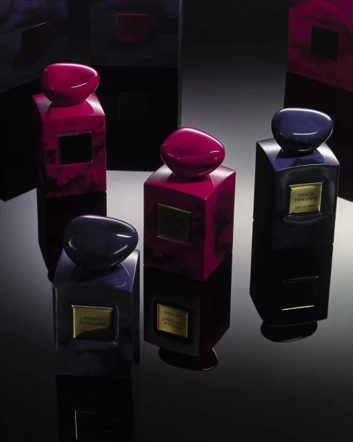Four Giorgio Armani Indigo Tanzanite perfume bottles with black and magenta colors on a glossy black surface reflecting studio lighting.