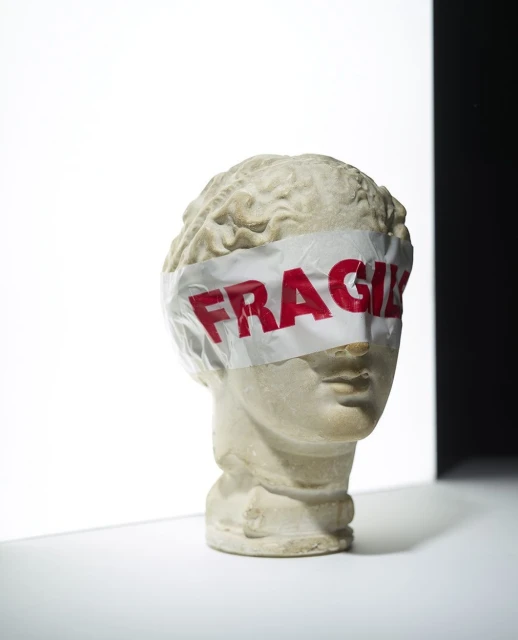 Still life studio shot of a bust sculpture with a fragile label covering the eyes, against a white and black background.