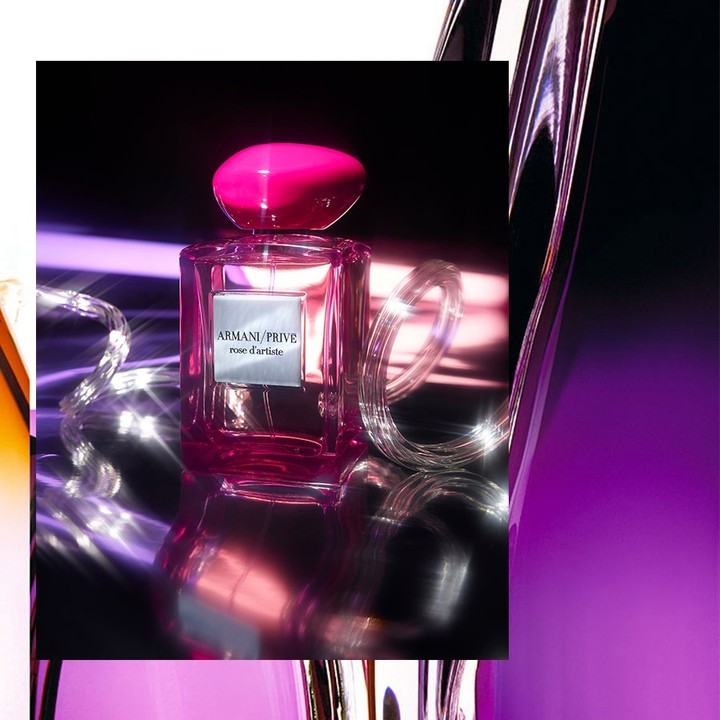 Armani Prive Rose D'Artiste perfume bottle with a pink cap, displayed on a black surface with silver wire lighting. 