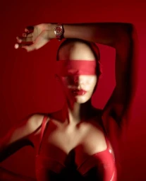 Model with red blindfold and glossy lips wearing a red top and wrist watch against a red background