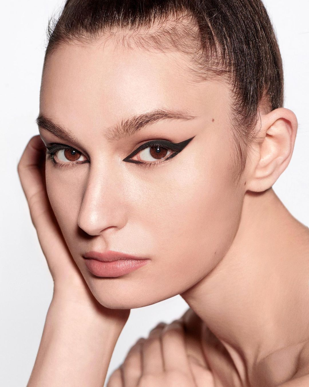 Close-up portrait of a woman with defined black eyeliner, showcasing beauty and makeup in a bright, clean studio environment.
