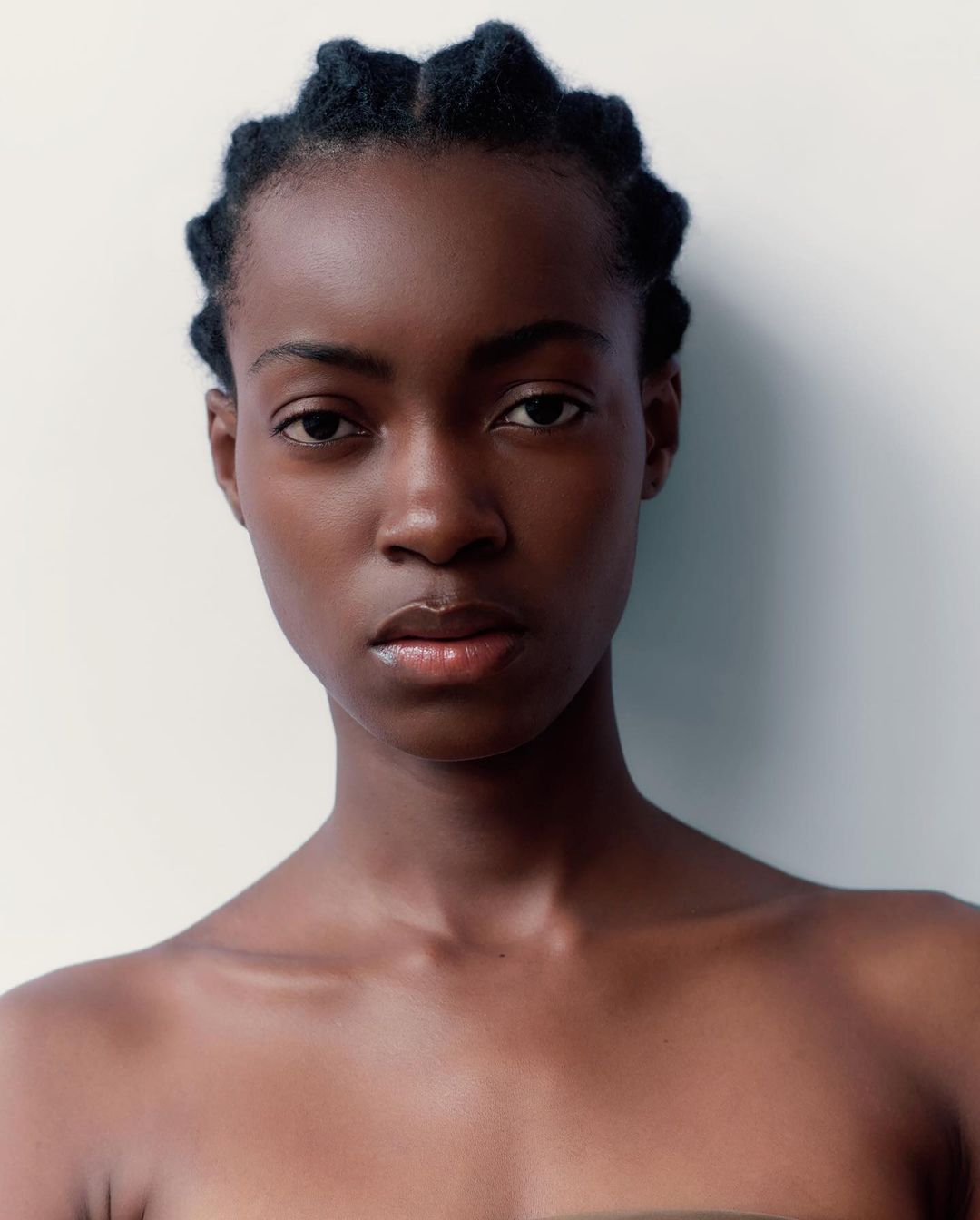 Close-up portrait of a young adult African woman with braided hair against a bright white background, highlighting natural beauty.