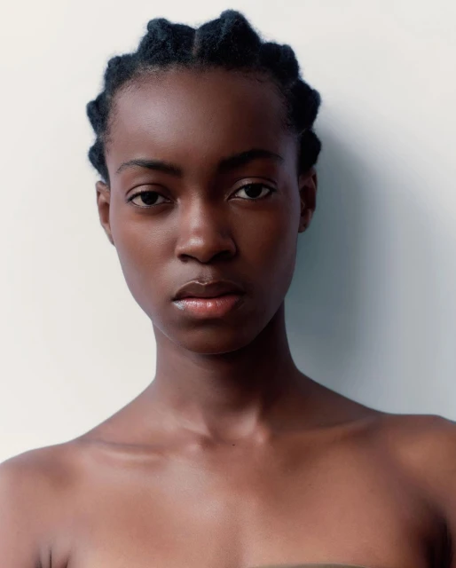 Close-up portrait of a young adult African woman with braided hair against a bright white background, highlighting natural beauty.