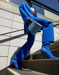 A person wearing a vibrant blue suit and blue boots ascends outdoor steps while holding a pale blue handbag.