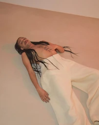 Man with long braided hair and mustache lying on a plain floor wearing light trousers, photographed by Daniela Müller-brunke