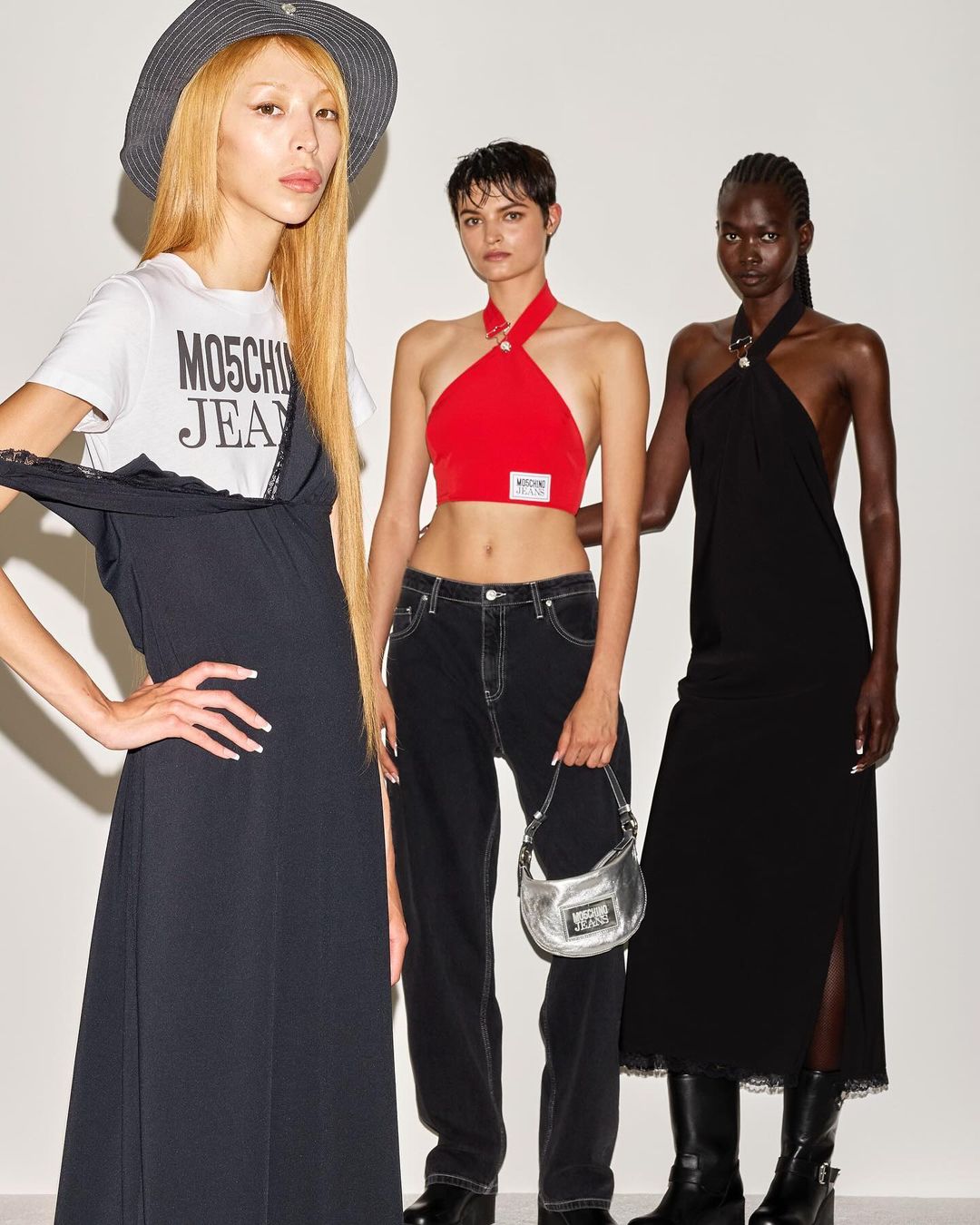 Three fashion models pose indoors against a white background, wearing garments from Moschino Jeans. One model wears a bucket hat.