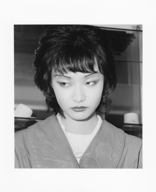 Monochrome portrait of a young woman with dark hair, soft makeup, and a serious expression, set against a neutral background.