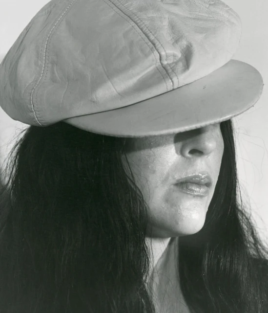 Monochrome portrait of an adult woman wearing a pale newsboy cap, with long dark hair against a neutral grey studio backdrop.