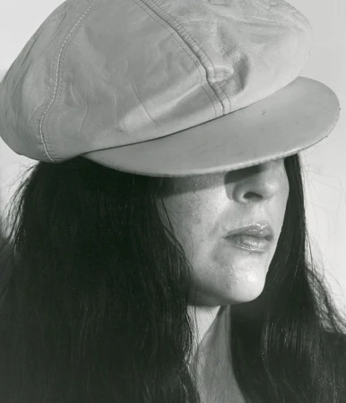 Monochrome portrait of an adult woman wearing a pale newsboy cap, with long dark hair against a neutral grey studio backdrop.