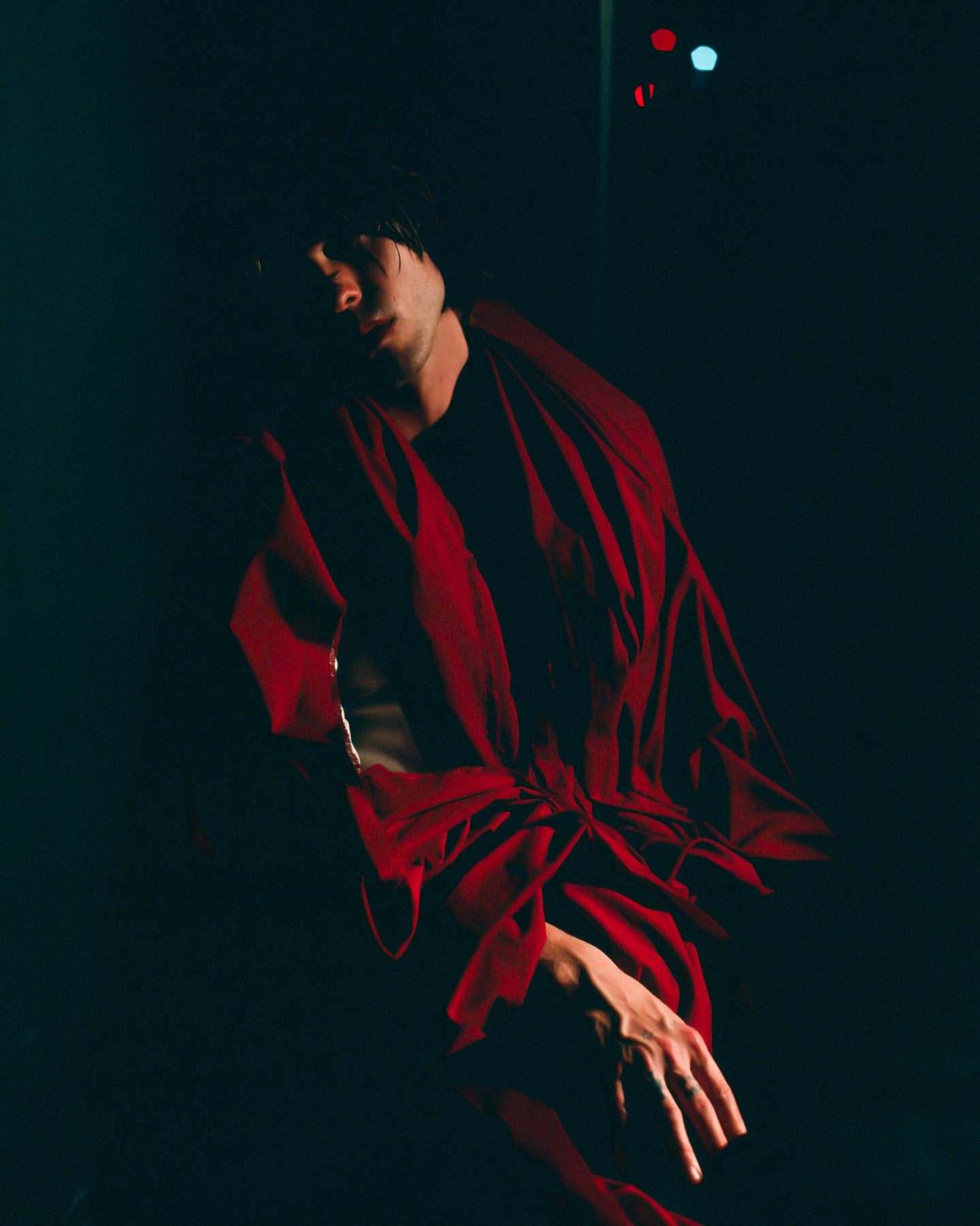 Person in red robe poses in dark studio with moody lighting. Dramatic fashion shot.
