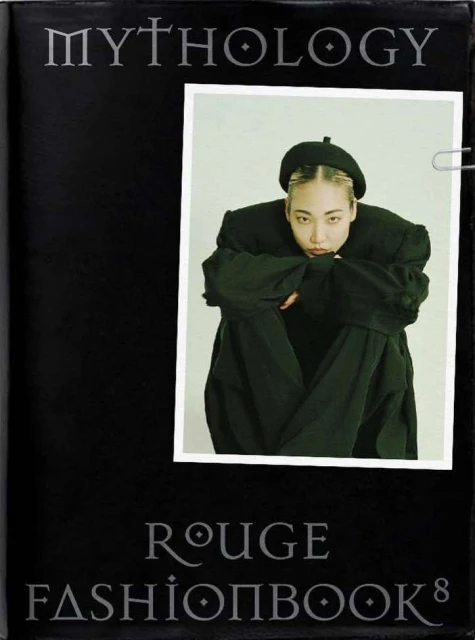 Fashion book cover featuring a portrait of an Asian woman wearing black clothing and a black beret, pinned inside the book with a paperclip.