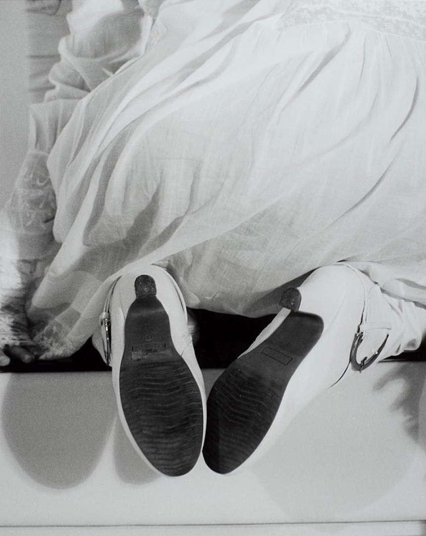 Low angle monochrome shot of white heeled shoes with textured soles worn with a white dress