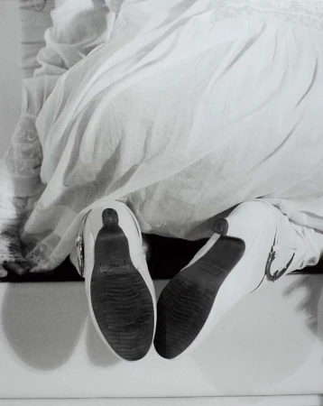 Low angle monochrome shot of white heeled shoes with textured soles worn with a white dress