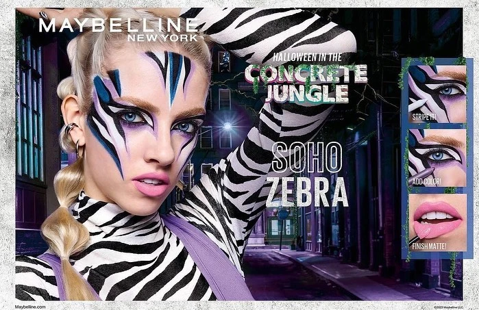 A woman is featured in a Maybelline cosmetics ad with zebra face paint, styled in a concrete jungle theme for Halloween, showcasing bold makeup.