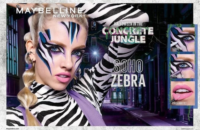 A woman is featured in a Maybelline cosmetics ad with zebra face paint, styled in a concrete jungle theme for Halloween, showcasing bold makeup.
