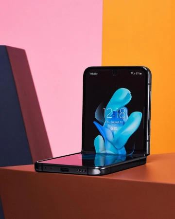 Foldable smartphone on a gradient background featuring a black border, displaying a vibrant blue and white abstract graphic design on its screen.