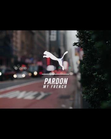 Puma logo with "Pardon My French" text displayed on a city street with blurred buildings and vehicles in the background.