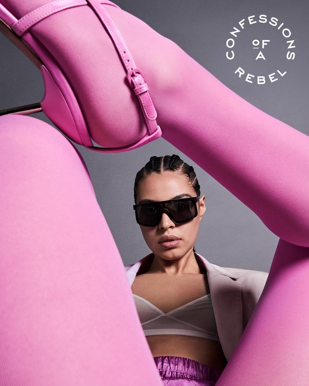 Eye-level shot of a woman in sunglasses and pink clothing, with a woman's leg and pink high-heeled shoe in the foreground.