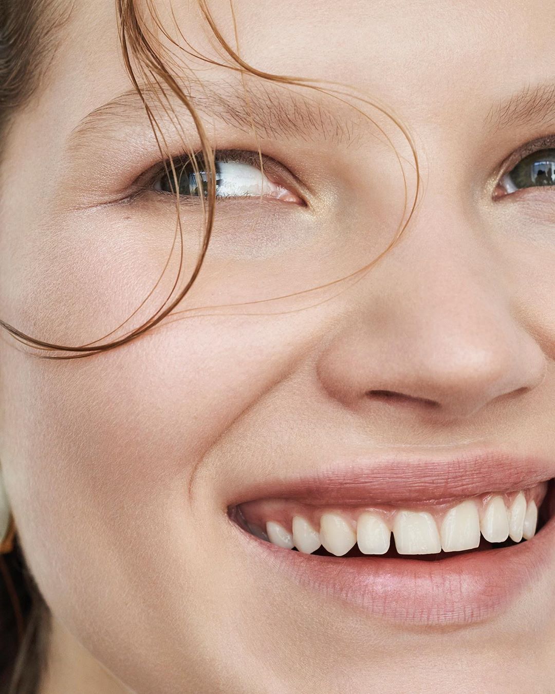 Close-up portrait of a smiling fair-skinned adult female with light brown hair, focusing on her expressive eyes and skin texture.