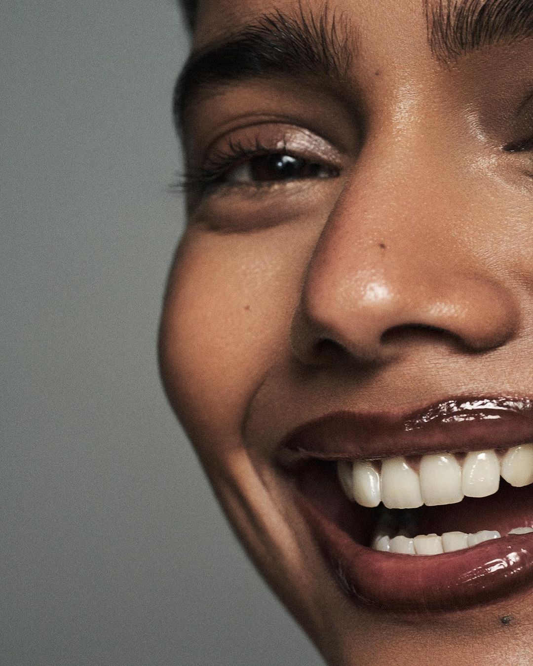 Close-up portrait of a smiling dark-skinned adult woman with a joyful expression, glossy lips, and an eye looking at the camera.