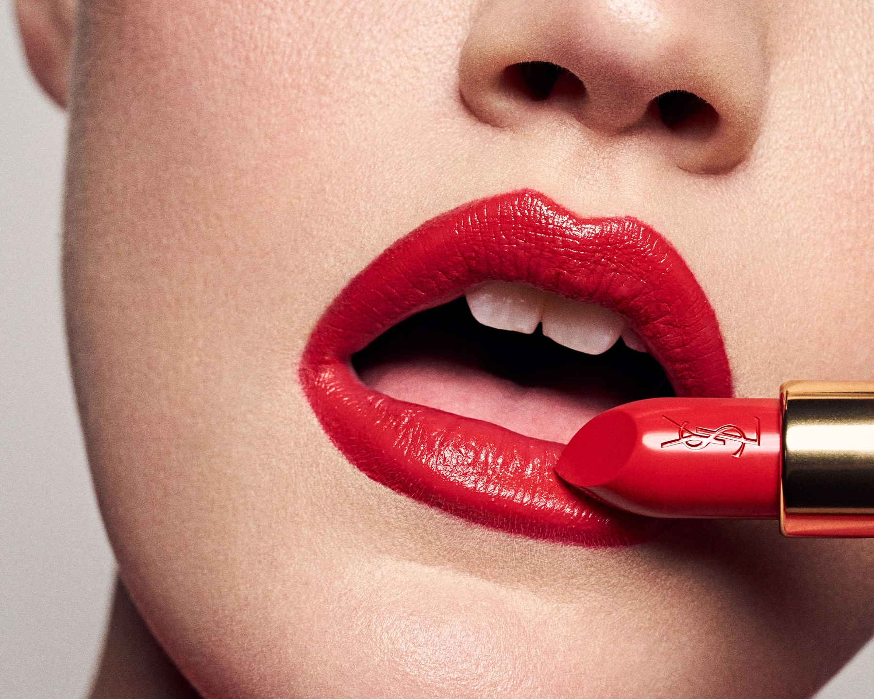 Close-up of a woman's face with bright red lipstick being applied. Features include the lips, teeth, and lipstick tube.