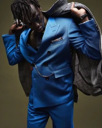 Black man with dreadlocks wearing a vibrant blue double-breasted suit and holding a houndstooth coat draped over his shoulders.
