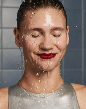 Close up portrait of a woman with wet hair and red lipstick as water splashes across her face