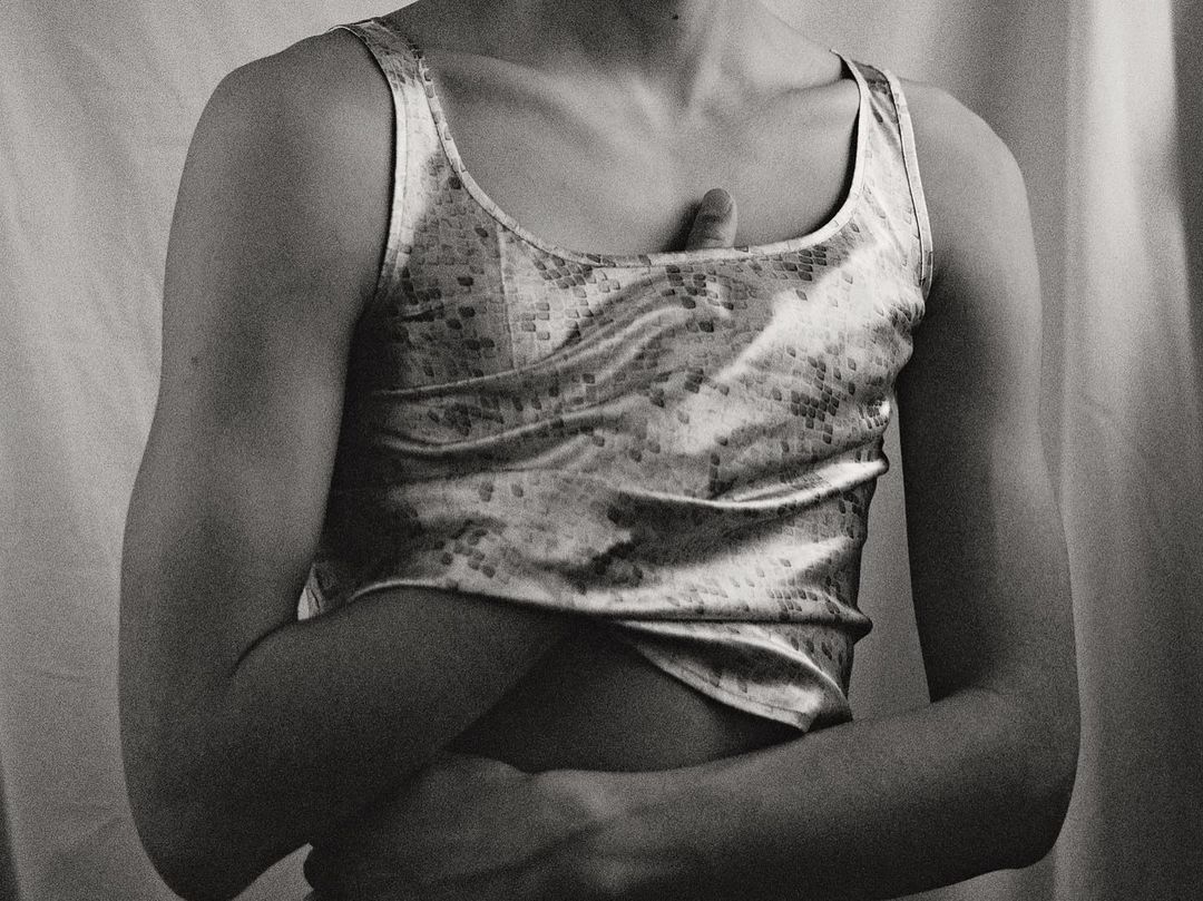 Monochrome portrait of a person wearing a patterned tank top against draped fabric background by Daniyel Lowden