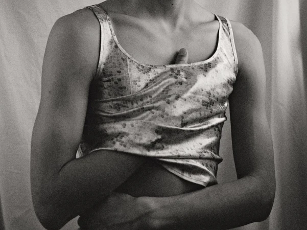 Monochrome portrait of a person wearing a patterned tank top against draped fabric background by Daniyel Lowden